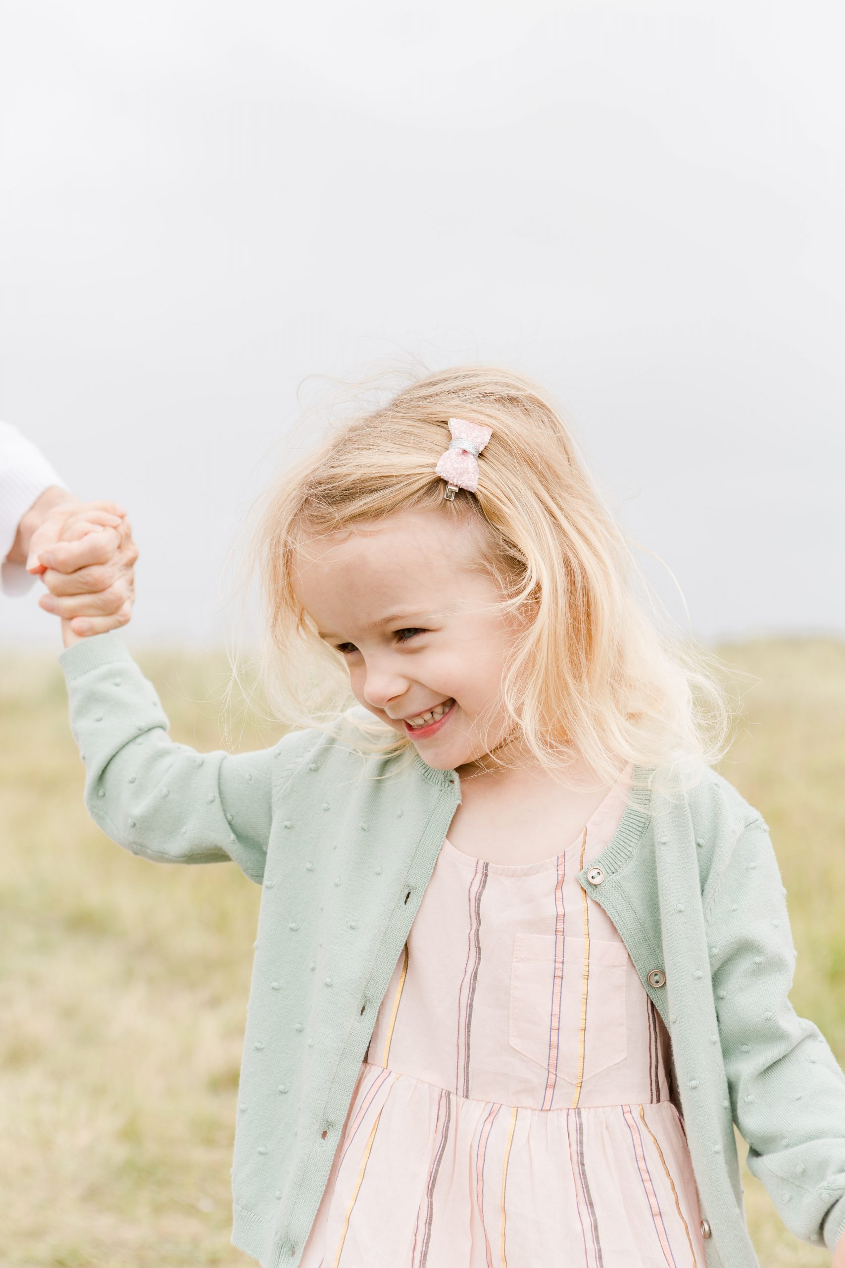 little girl holding adults hand smiling down at the ground