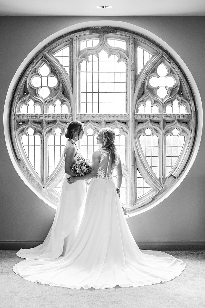 two brides stood in front of rounds church window