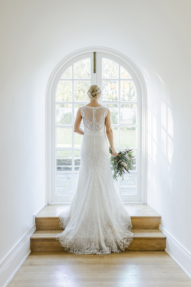 bride stood in arched window holing bouquet