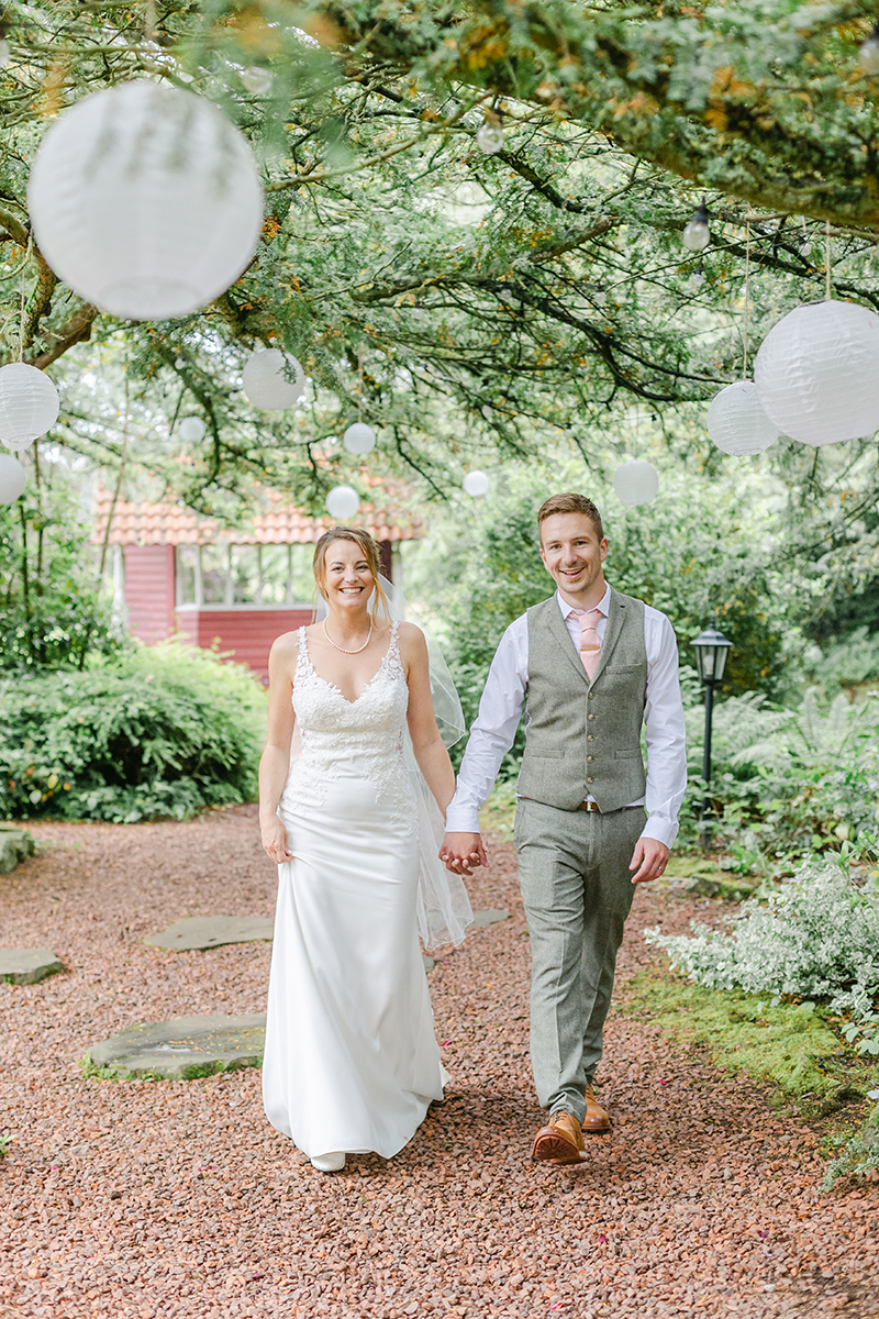 bride and groom walking through woods with paper lanterns