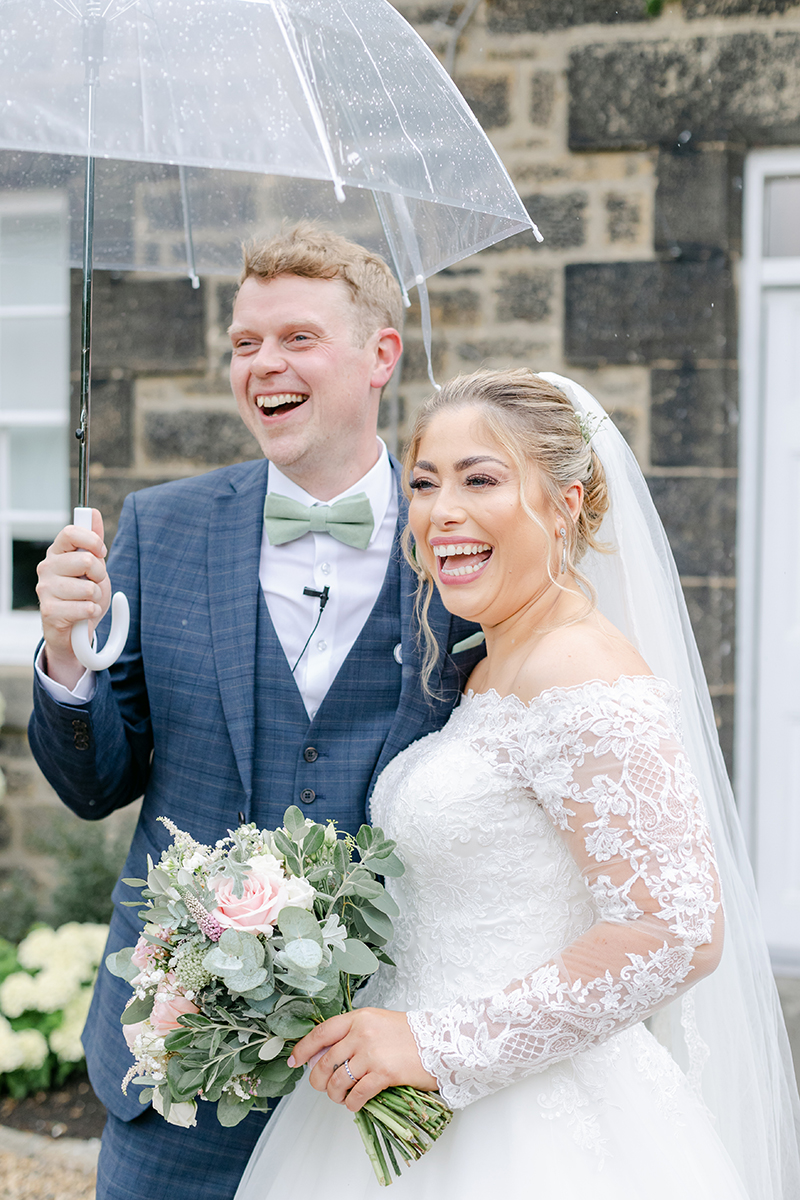 Bride and groom laughing under clear umbrella