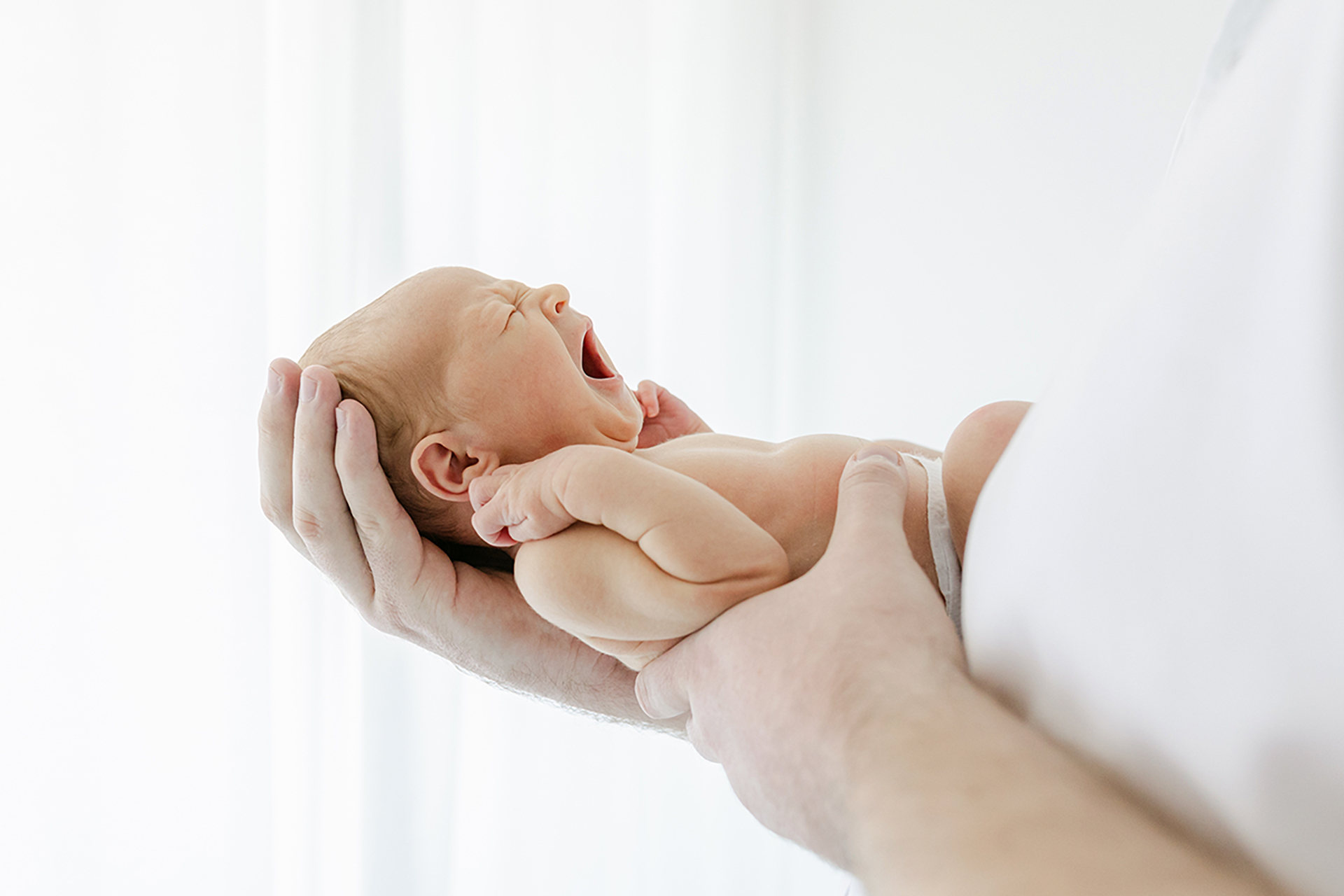 newborn held on dads arm and yawning