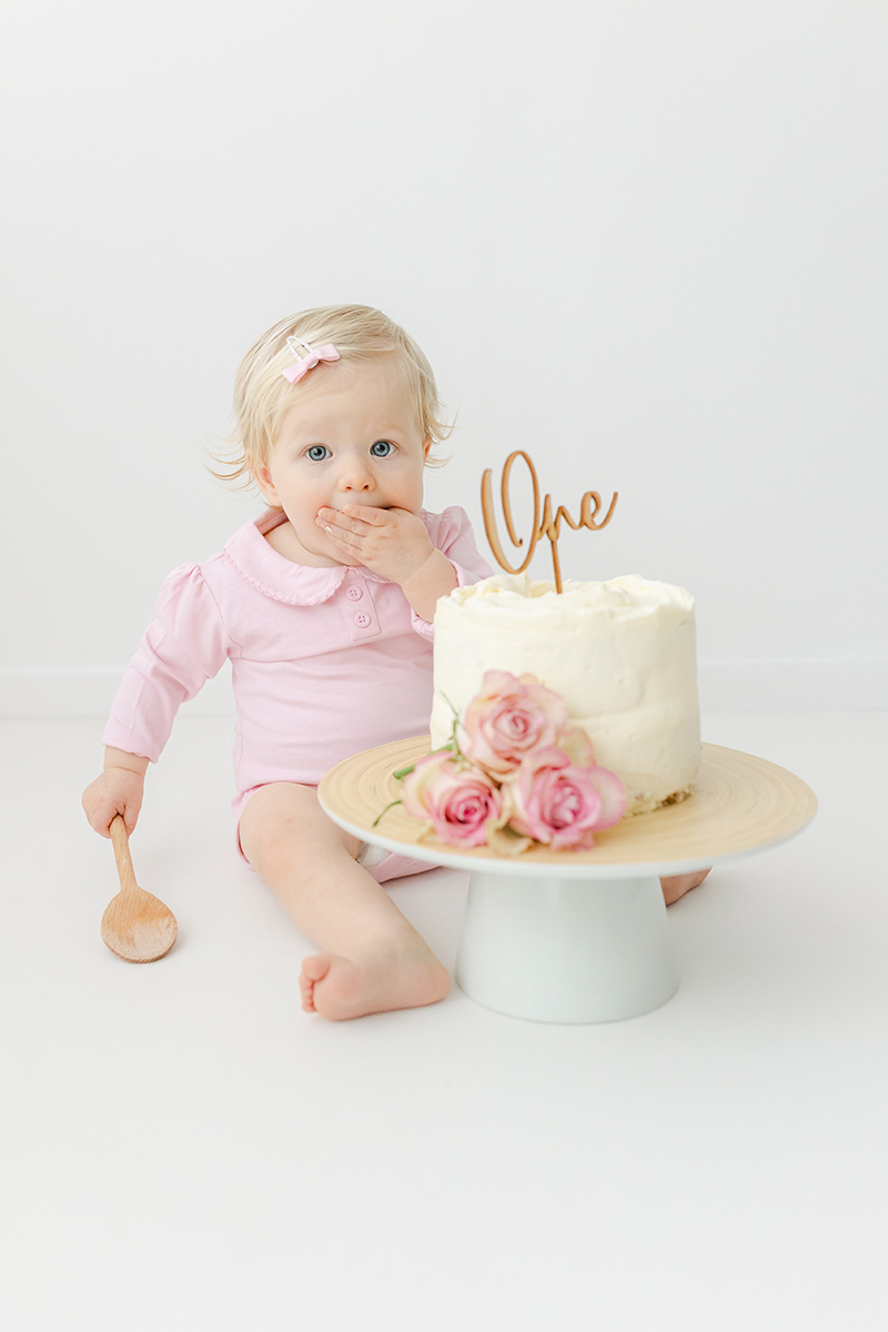 little girl eating 1st birthday cake in photo studio