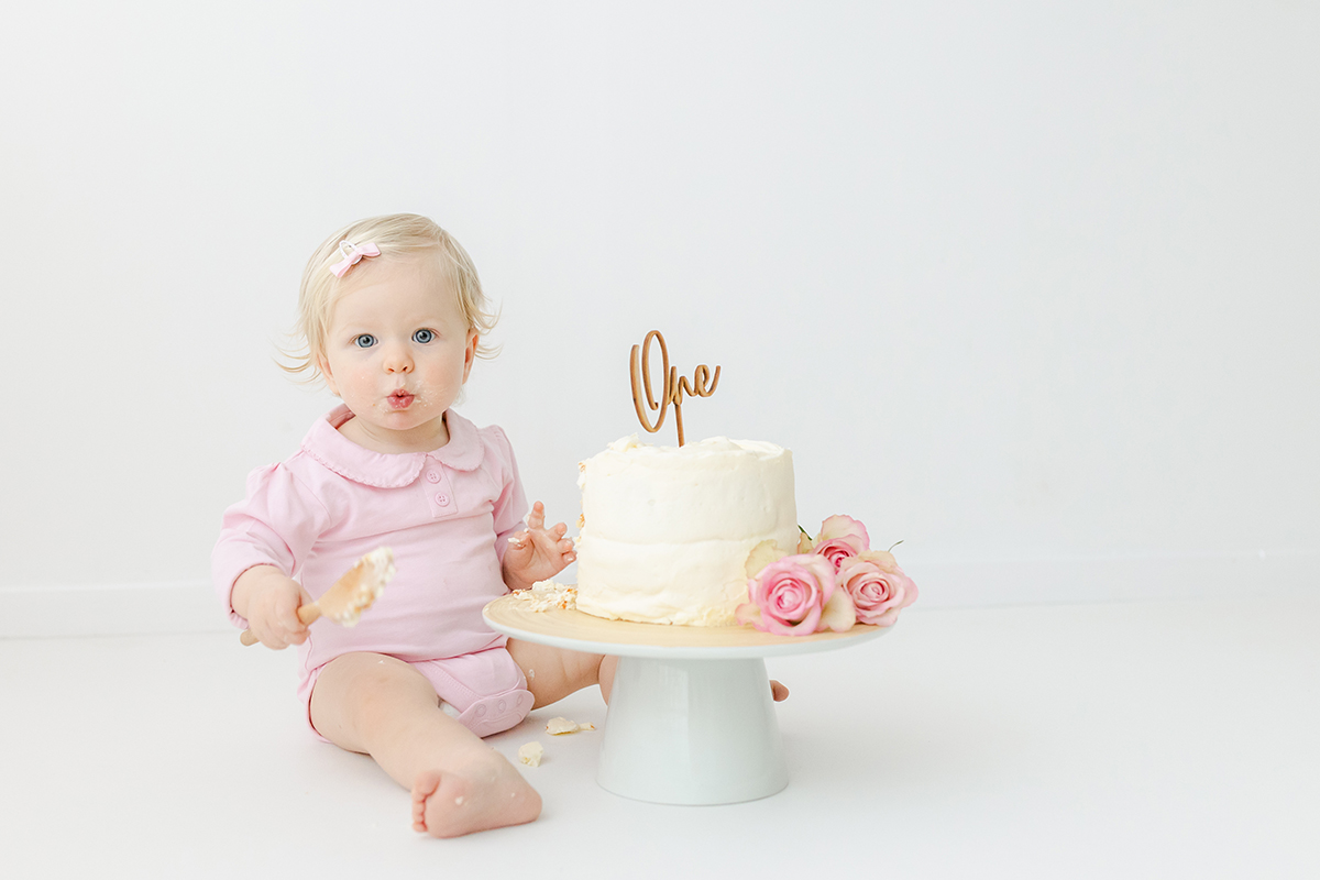 little girl eating 1st birthday cake blowing kisses