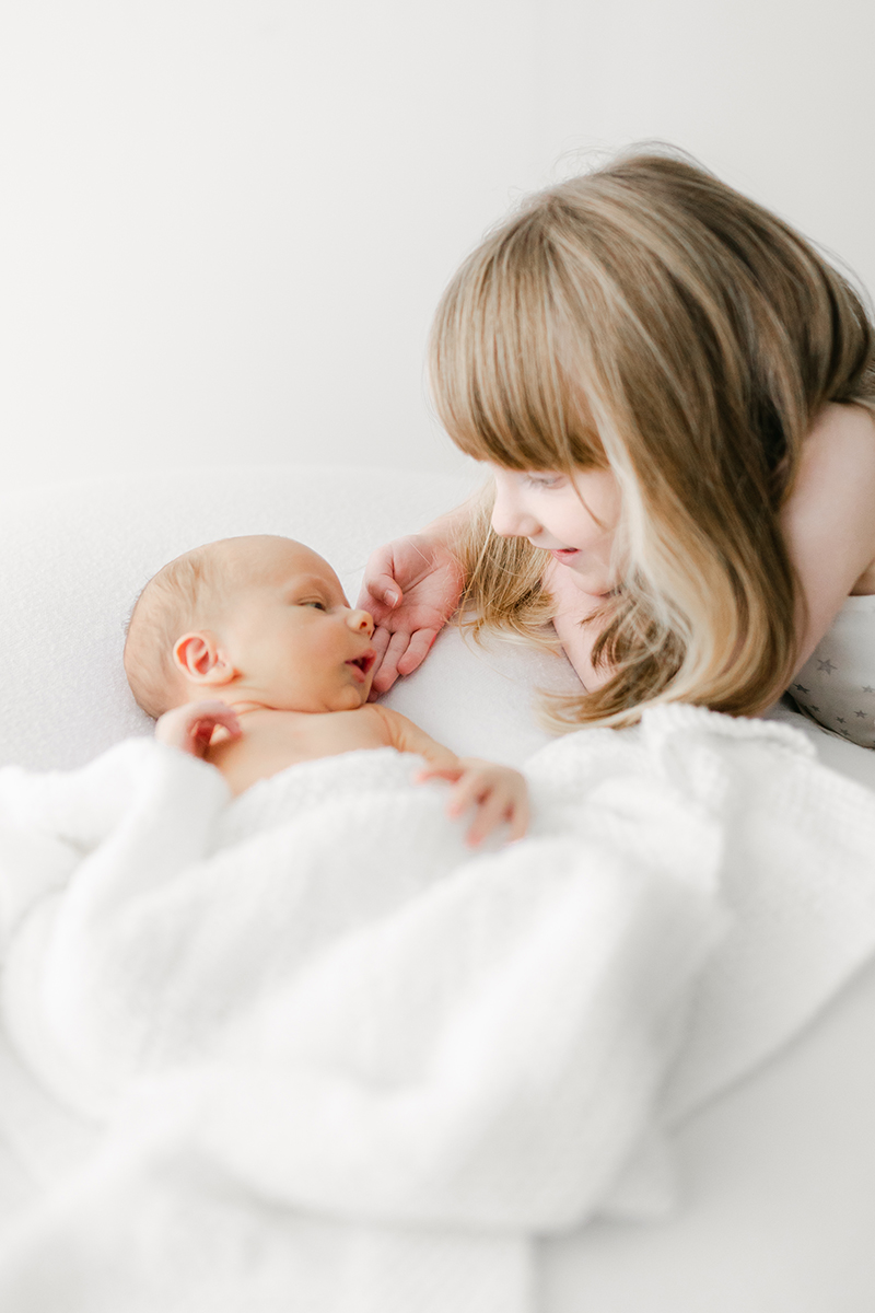 big sister smiling at baby and touching his cheek