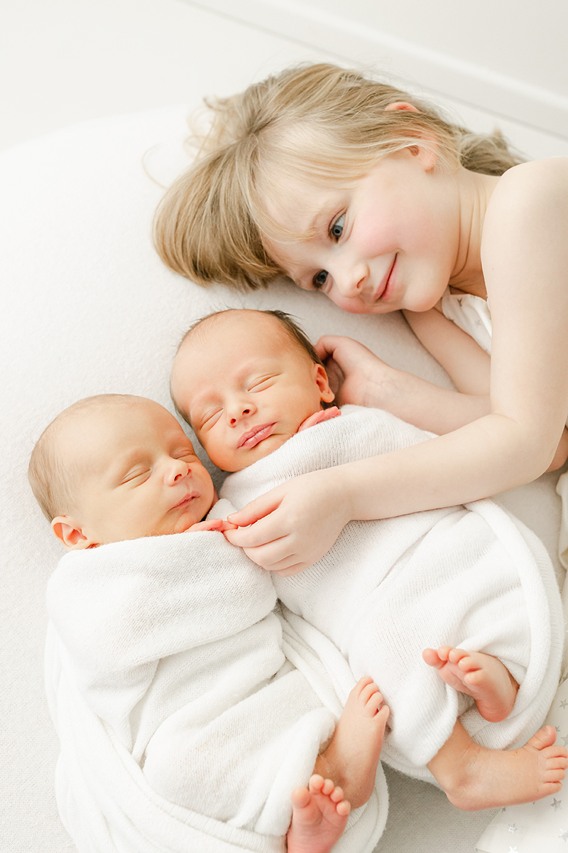 big sister lying next to twin brothers holding finger