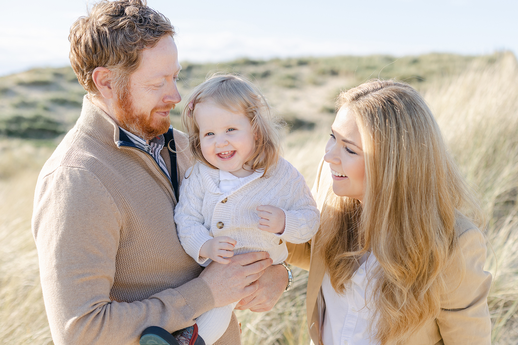 mum and dad smiling at daughter in dunes for family photo shoot