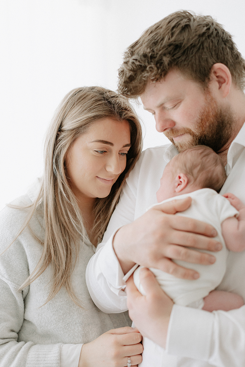 dad cuddling newborn mum looking over shoulder