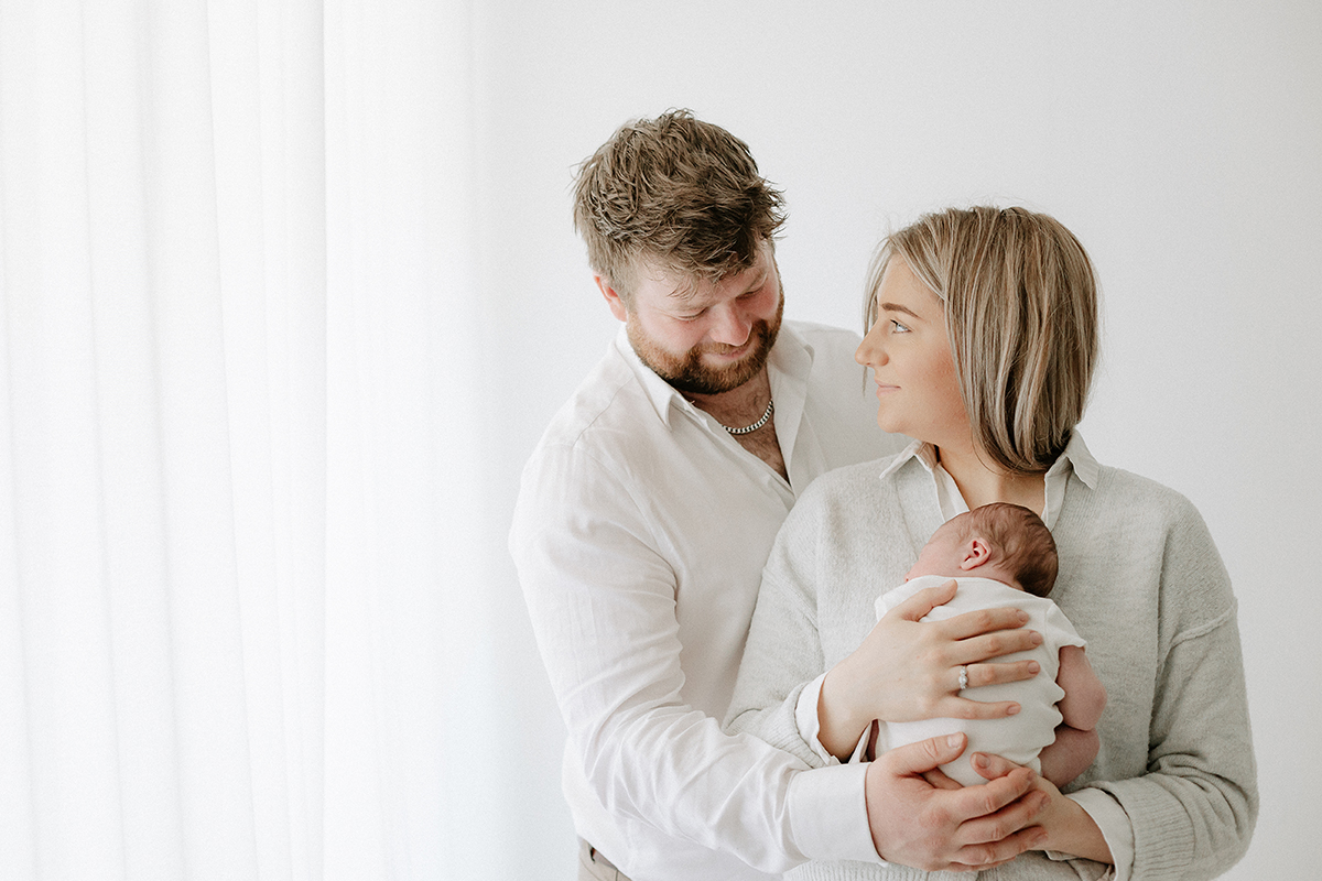 mum cuddling newborn dad looking over shoulder