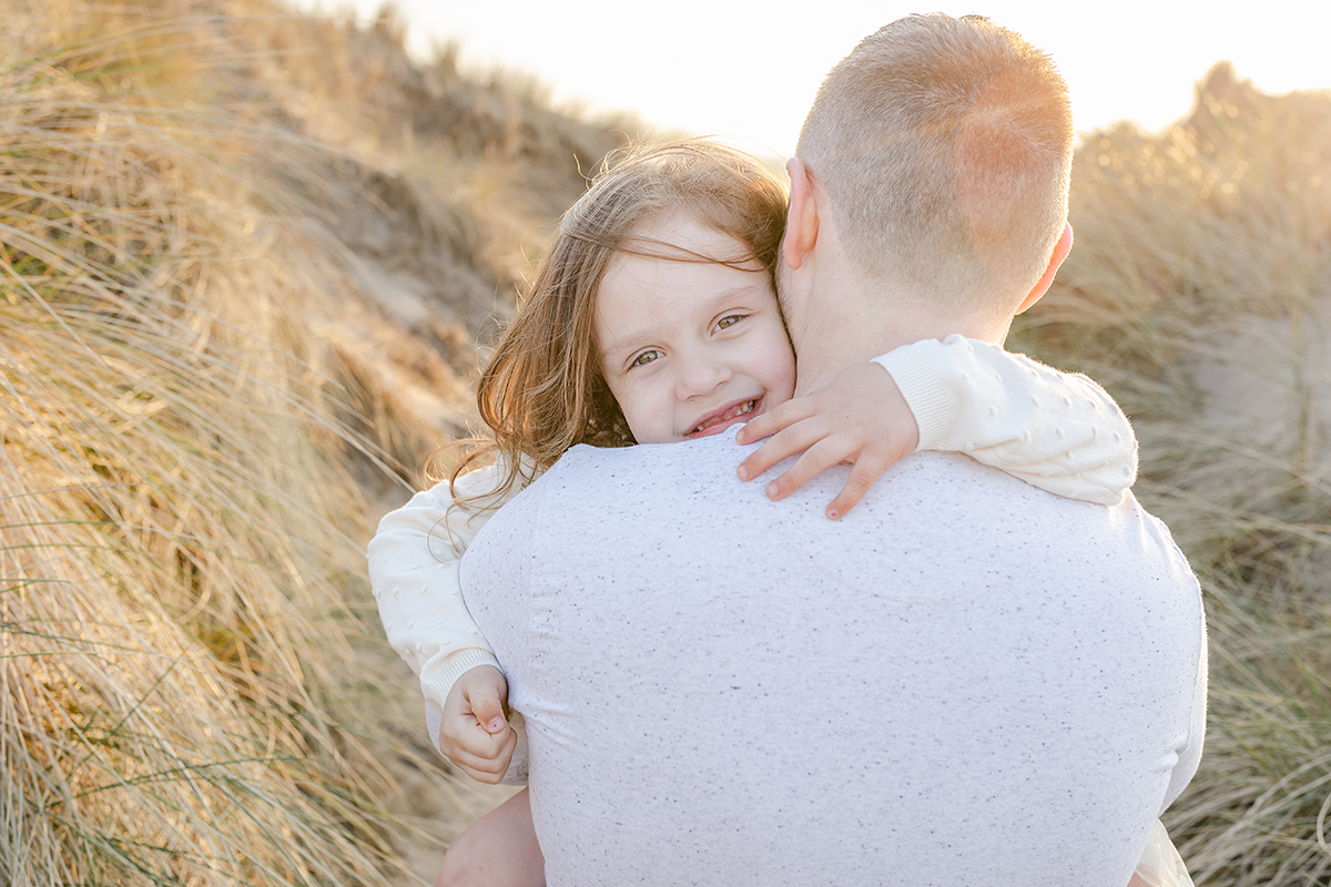 little girl smiling over dad's shoulder on the beach