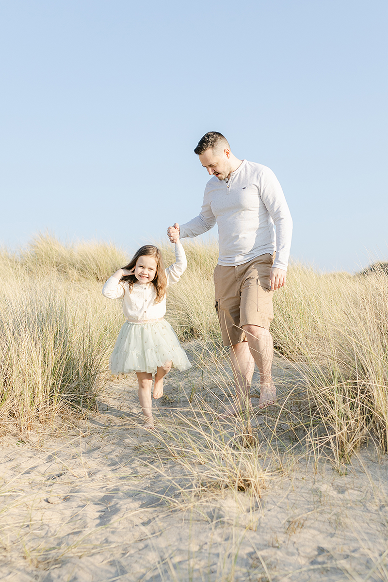 dad holding daughters hand through dunes