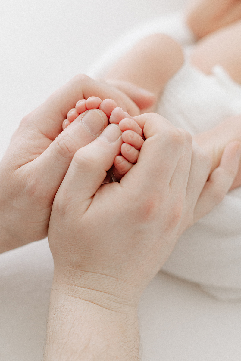 dad holding newborn feet with thumbs