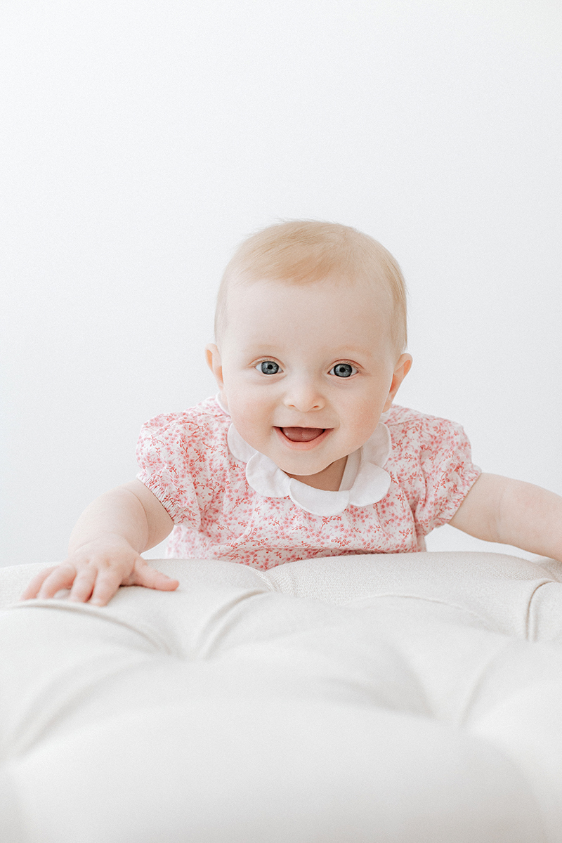 baby in pink holding on to stool smiling at camera