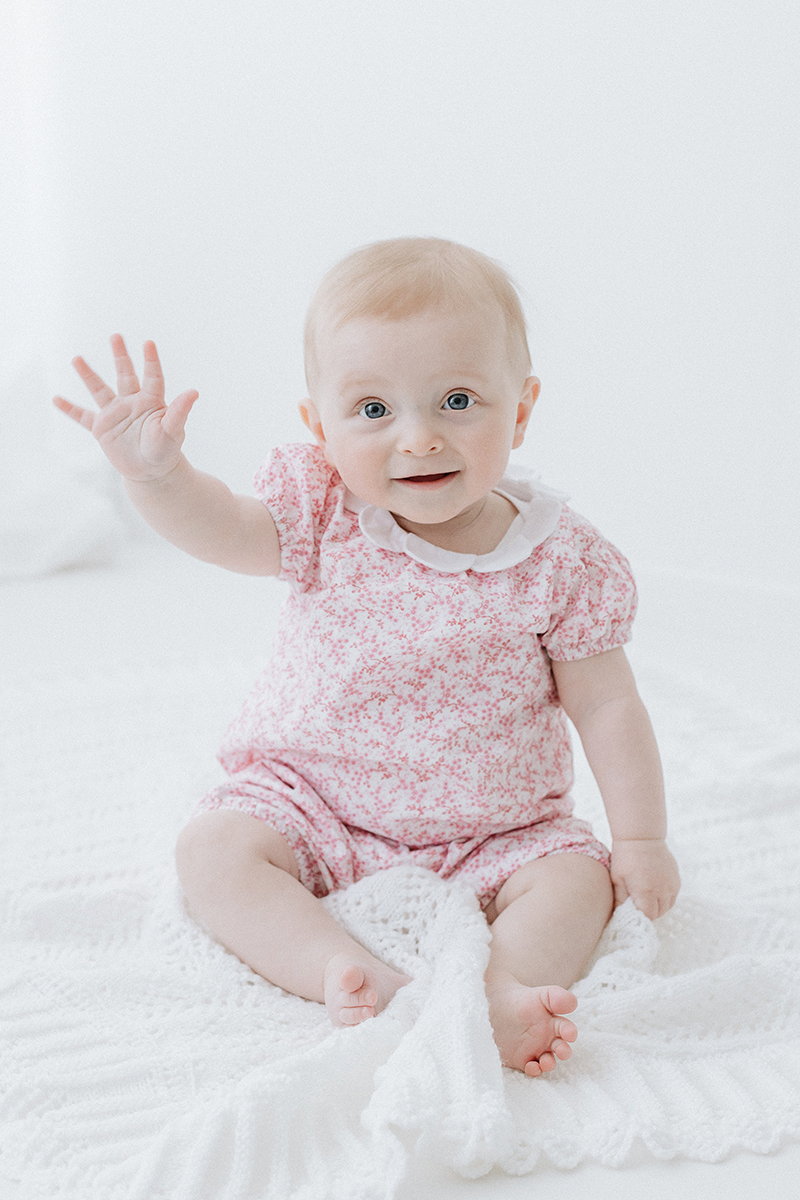 baby in pink sitting up and waving